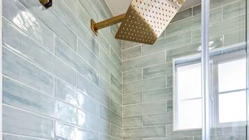 A shower with a glass door, a gold showerhead, and a tiled wall.