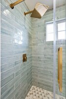 Chuveiro com porta de vidro, chuveiro com detalhes dourados e parede revestida de azulejos.