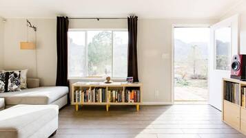 A modern living room with a sofa, a bookshelf, and a large window with curtains.