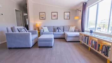 A modern living room with a sectional sofa, a small ottoman, and a bookshelf filled with books.