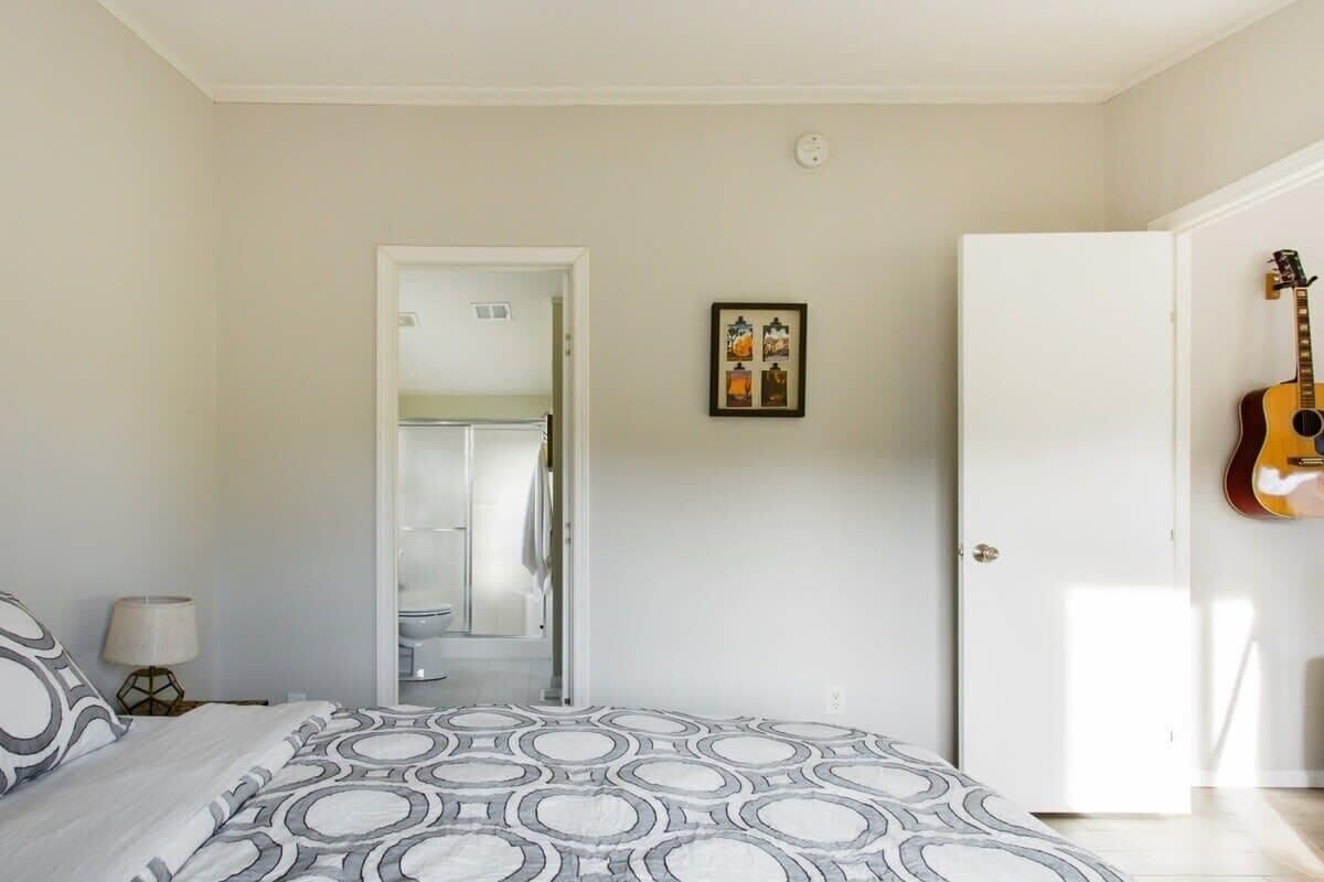 A bedroom with a bed, a guitar, and a door leading to a bathroom.