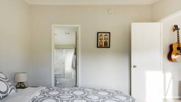 A bedroom with a bed, a guitar, and a door leading to a bathroom.