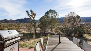 A barbecue grill and wooden deck overlooking a desert landscape with cacti and distant mountains.