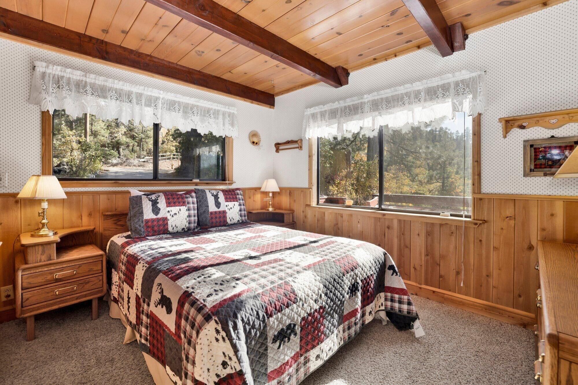 Um quarto com uma cama grande, duas mesas de cabeceira, uma janela com vista para árvores e paredes de madeira.