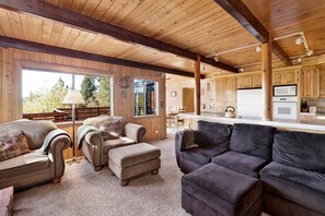 A cozy cabin interior with a wooden ceiling, a dining area, a kitchen with a microwave, and a large window offering a view of trees. - Mountain Hideaway On Maryland #2494 (Big Bear Lake)