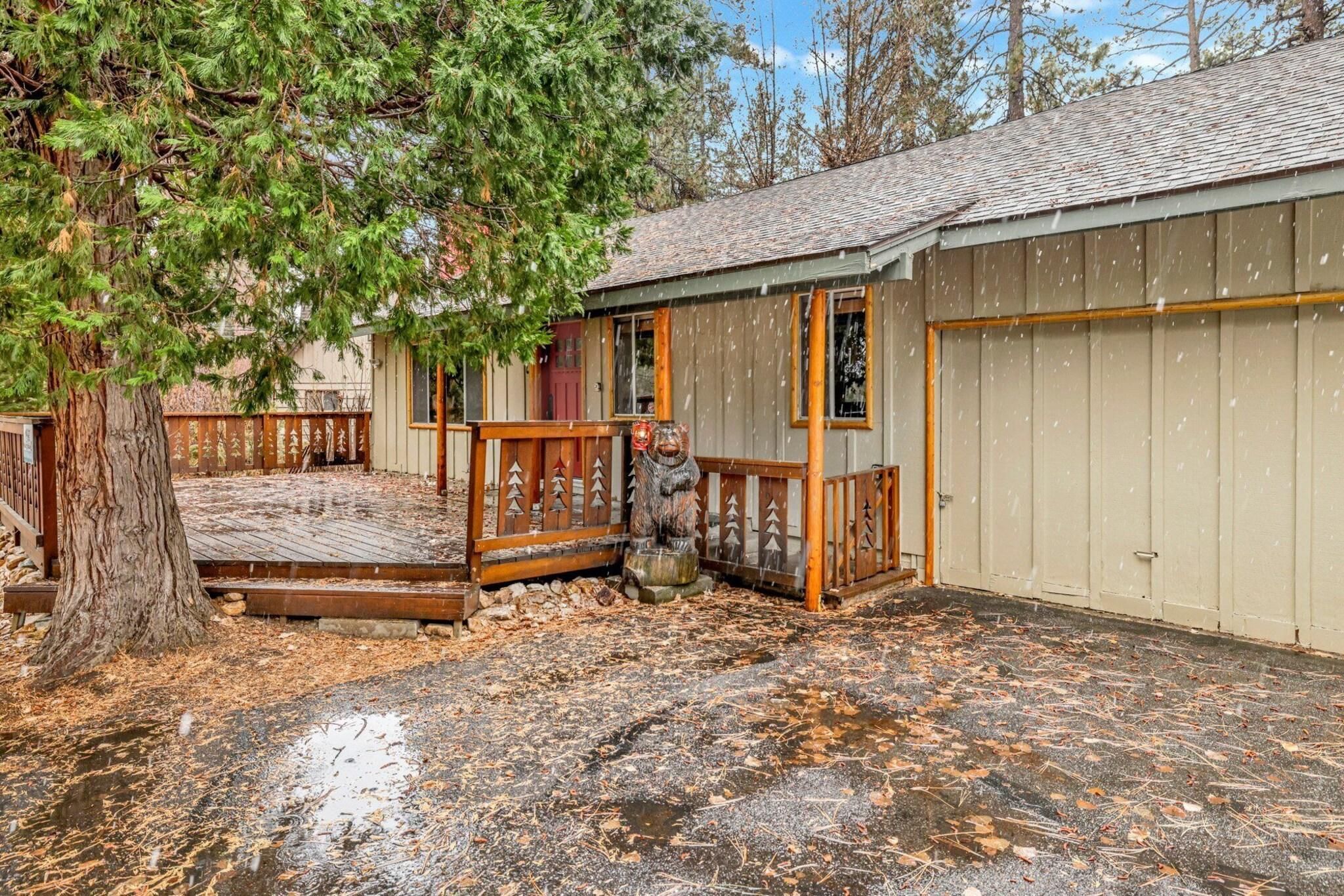 A wooden deck leading to a building with a garage, surrounded by trees and a leaf-covered ground.