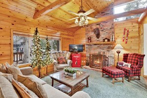 A cozy cabin interior with a fireplace, wooden walls, a television, and a Christmas tree. - Timber Pines Chalet #2417 (Big Bear Lake)