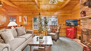 A cozy cabin interior with a wooden ceiling, a sofa, a chair, a coffee table, a television, and a fireplace. - Timber Pines Chalet #2417 (Big Bear Lake)