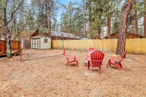 A backyard with a wooden deck, a small shed, and red Adirondack chairs.