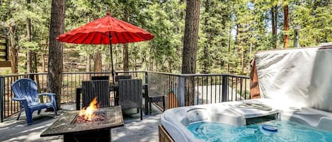 A hot tub with a wooden deck, a fire pit, and outdoor seating.