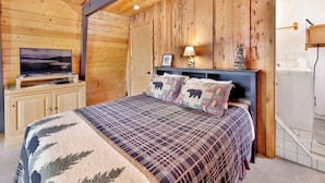 A bedroom with a bed, a television, and wooden walls.