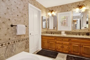 Un bagno con una vasca da bagno bianca, armadietti in legno, uno specchio grande e un porta asciugamani.