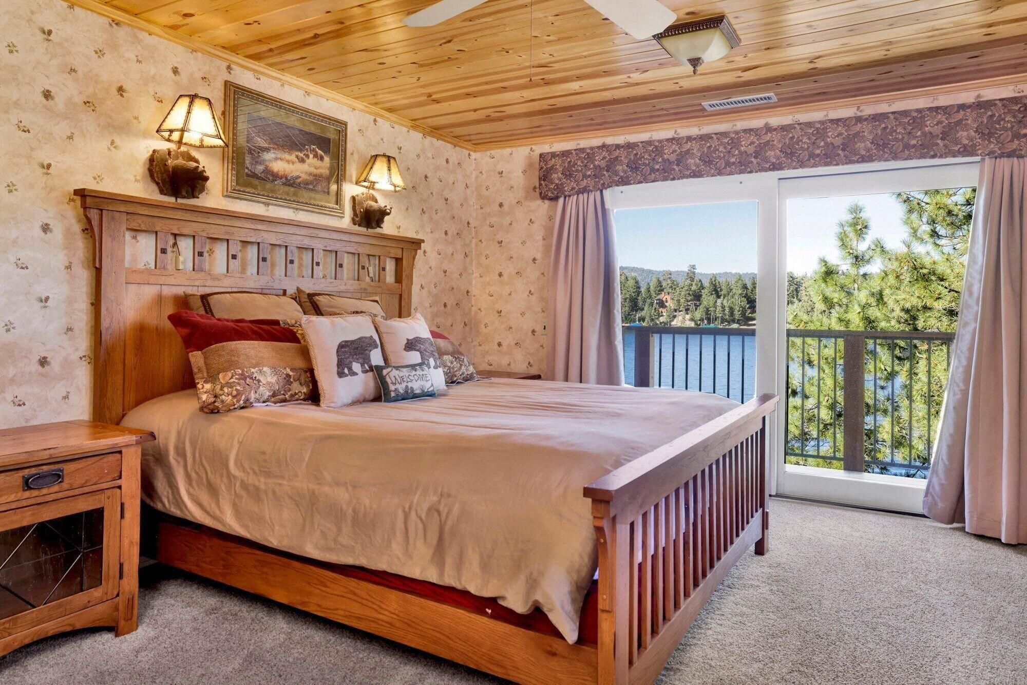 A wooden-framed bed with a headboard, a nightstand, and a window with a view of trees and a lake.