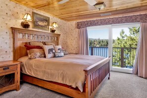 Un letto con struttura in legno, una testiera, un comodino e una finestra vista alberi e lago.