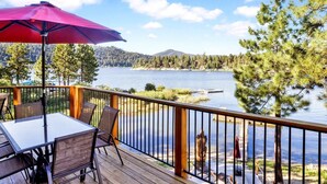 A deck with a table and chairs, overlooking a lake with trees and a mountain in the background. - Cove Lakefront Chalet #2098 (Big Bear Lake)