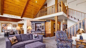 A spacious living area with a high ceiling, a wooden staircase, and a cozy seating arrangement. - Cove Lakefront Chalet #2098 (Big Bear Lake)
