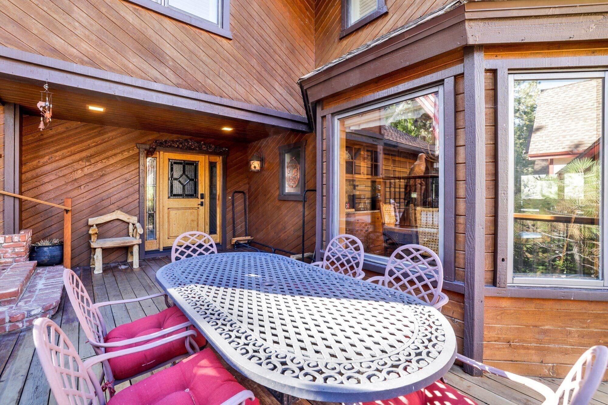 Eine Holzterrasse mit einem Metalltisch und -stühlen, eine Tür mit Glasfenster und ein Blick durch große Fenster.