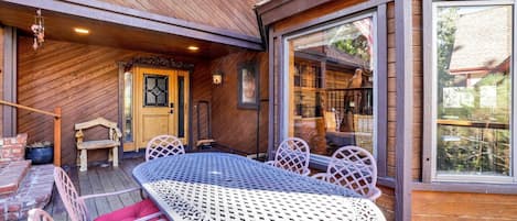 Eine Holzterrasse mit einem Metalltisch und -stühlen, eine Tür mit Glasfenster und ein Blick durch große Fenster.