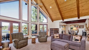 A spacious living room with large windows, a high ceiling, and a cozy fireplace. - Cove Lakefront Chalet #2098 (Big Bear Lake)
