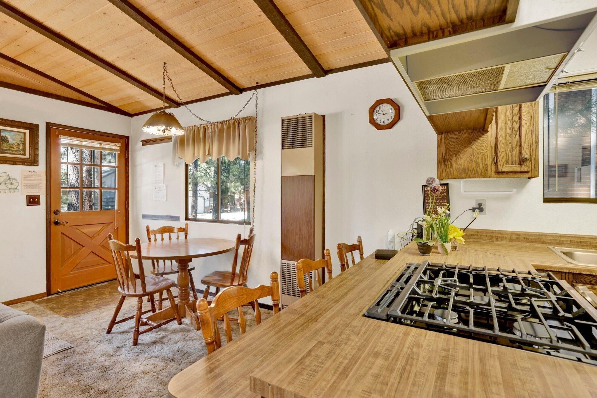A dining area with a wooden table and chairs, a kitchen with a stove, and a clock on the wall.