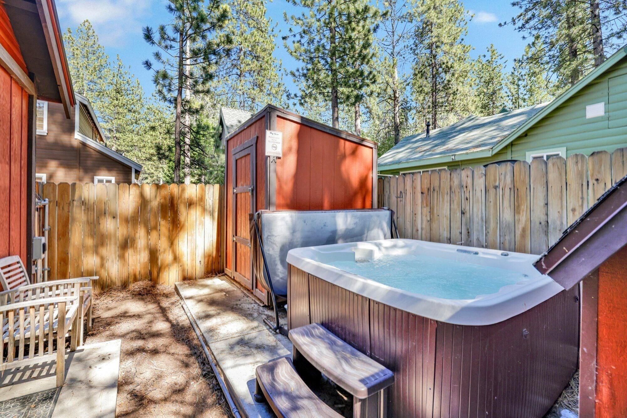 A backyard with a hot tub, wooden deck, and a fenced area.
