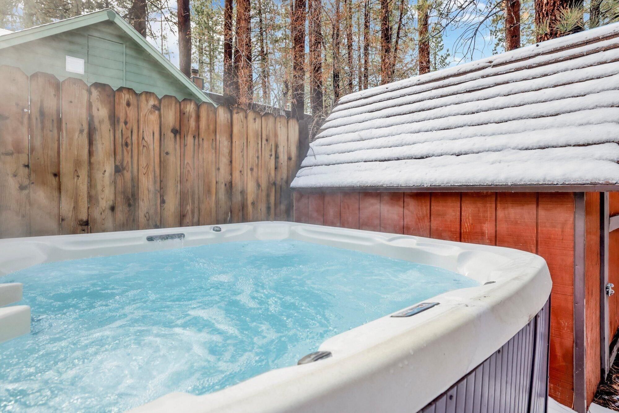 A hot tub with a wooden fence and a snow-covered roof in a backyard.