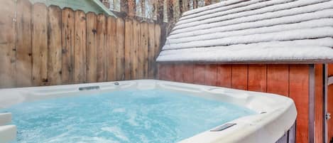 A hot tub with a wooden fence and a snow-covered roof in a backyard.