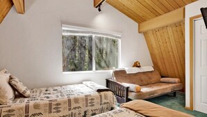 Un dormitorio con dos camas, una ventana con vistas a árboles, techo de madera y una puerta.