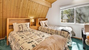 Una habitación con dos camas, paredes de madera, una ventana con vistas y una silla.