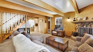 Un salón amplio con una escalera de madera, una chimenea de piedra y un televisor.