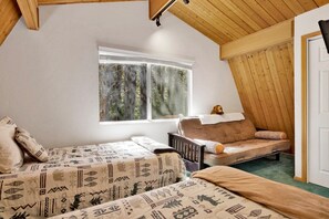 A bedroom with two beds, a window with a view of trees, a wooden ceiling, and a door. - Our Cabin In The Woods #2476 (Big Bear Lake)