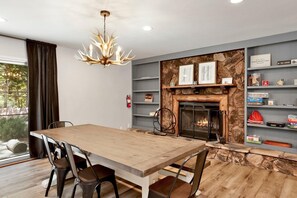 A dining area with a wooden table and chairs, a fireplace, and a stone wall with shelves. - Wildwood Lodge #2087 (Big Bear Lake)