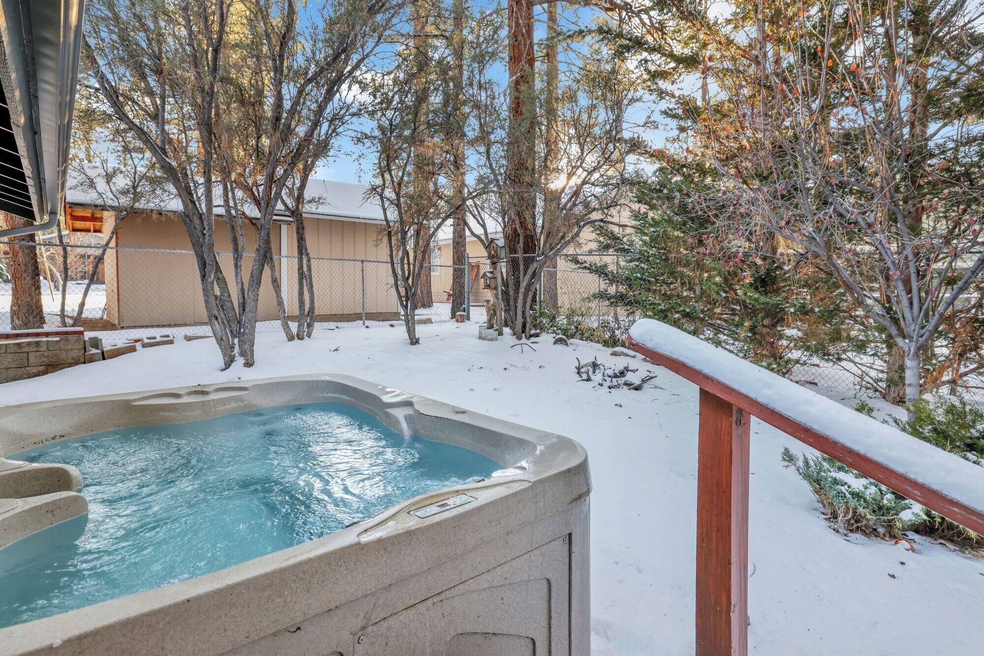 Una vasca idromassaggio in una zona esterna innevata, con alberi e un edificio sullo sfondo.