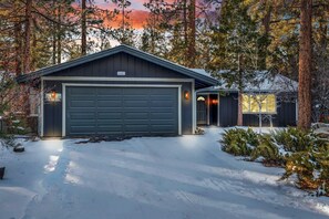 Een garage voor twee auto's met een donker dak, omgeven door met sneeuw bedekte grond en bomen.