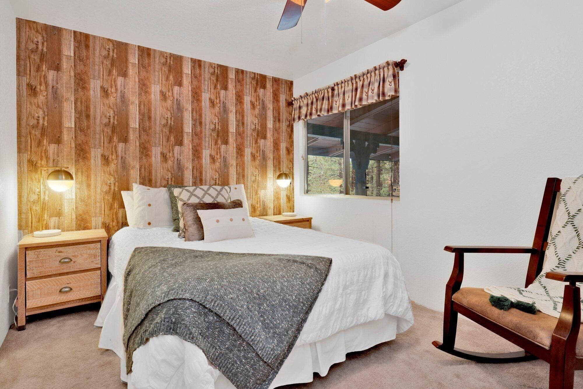 Un dormitorio con cabecera de madera, cama con ropa de cama blanca, mesita de noche con lámpara y ventana con vistas.