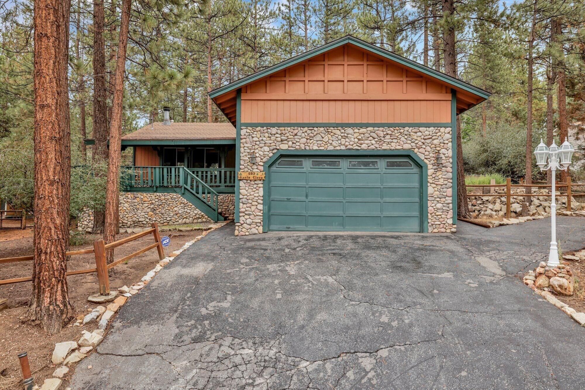 A two-story building with a stone facade and a green garage door, surrounded by trees.
