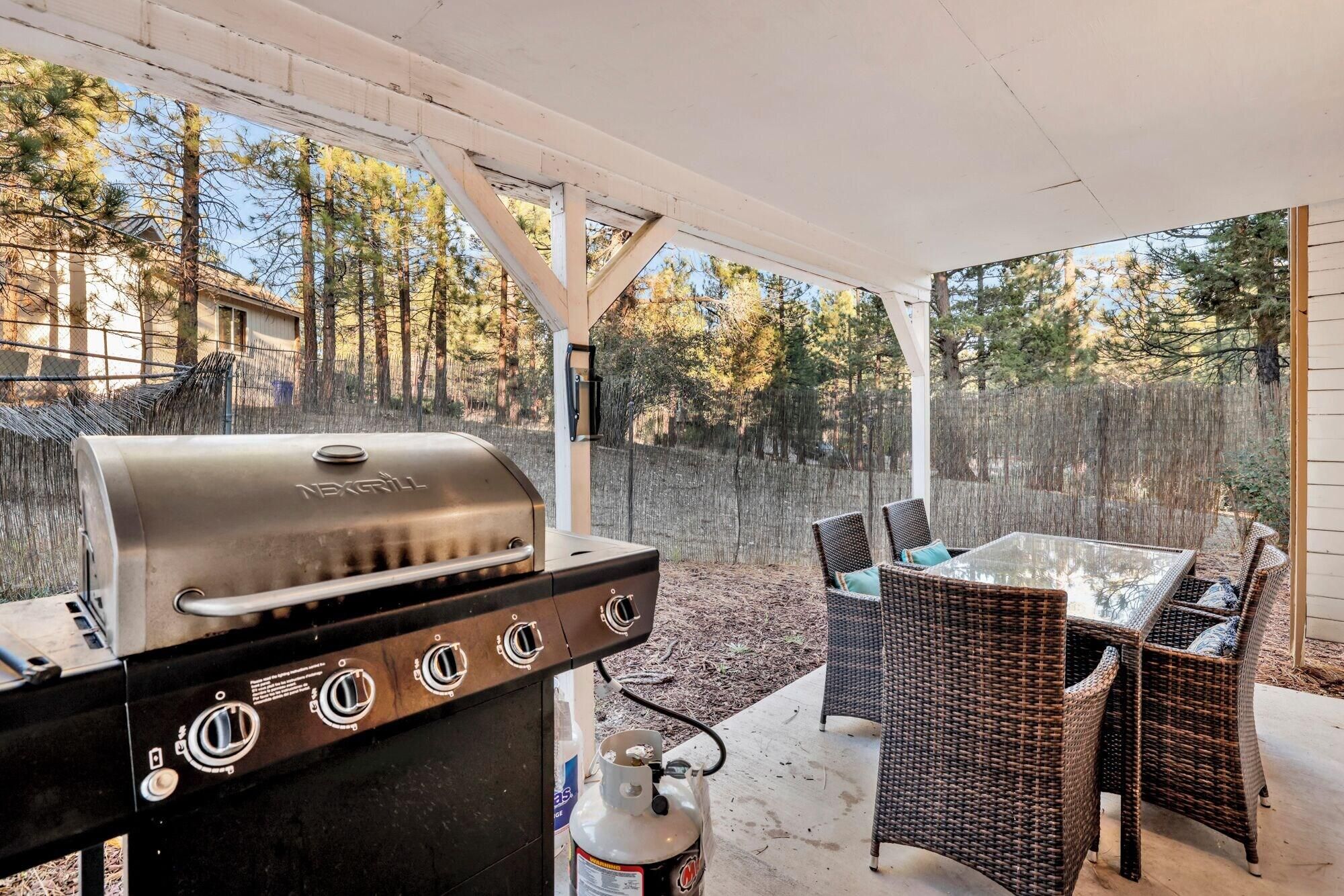 An outdoor patio with a grill, wicker furniture, and a view of trees.