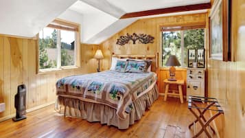 A cozy bedroom with a wooden ceiling, a bed with a patterned bedspread, a nightstand with a lamp, and a dresser with a mirror.