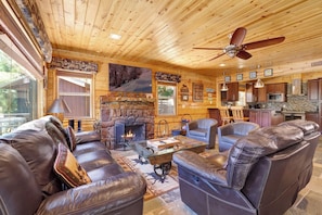 A log cabin interior with a fireplace, leather furniture, and a kitchen area. - Circle Views #1602 (Big Bear Lake)