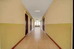 A long, narrow hallway with doors on both sides, leading to a bright room at the end. - Hotel O Depok Near Bhayangkara Brimob Hospital (Depok)