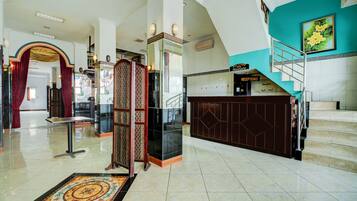 A hotel lobby with a reception desk, a staircase, and a patterned floor.