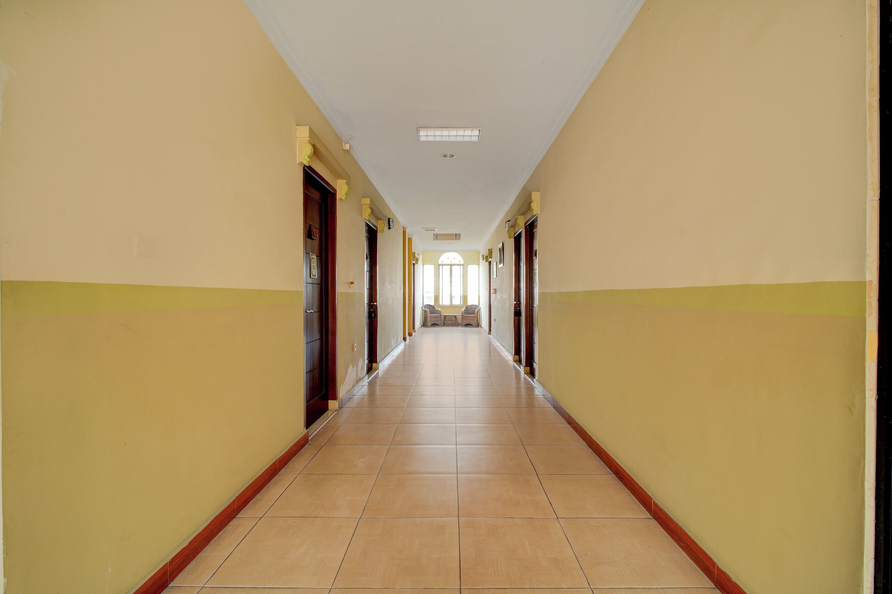 Un pasillo largo y estrecho con puertas a ambos lados, que conduce a una habitación luminosa al final.