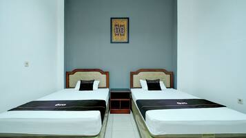 A hotel room with two single beds, a small table, a wall-mounted shelf, and a framed picture.