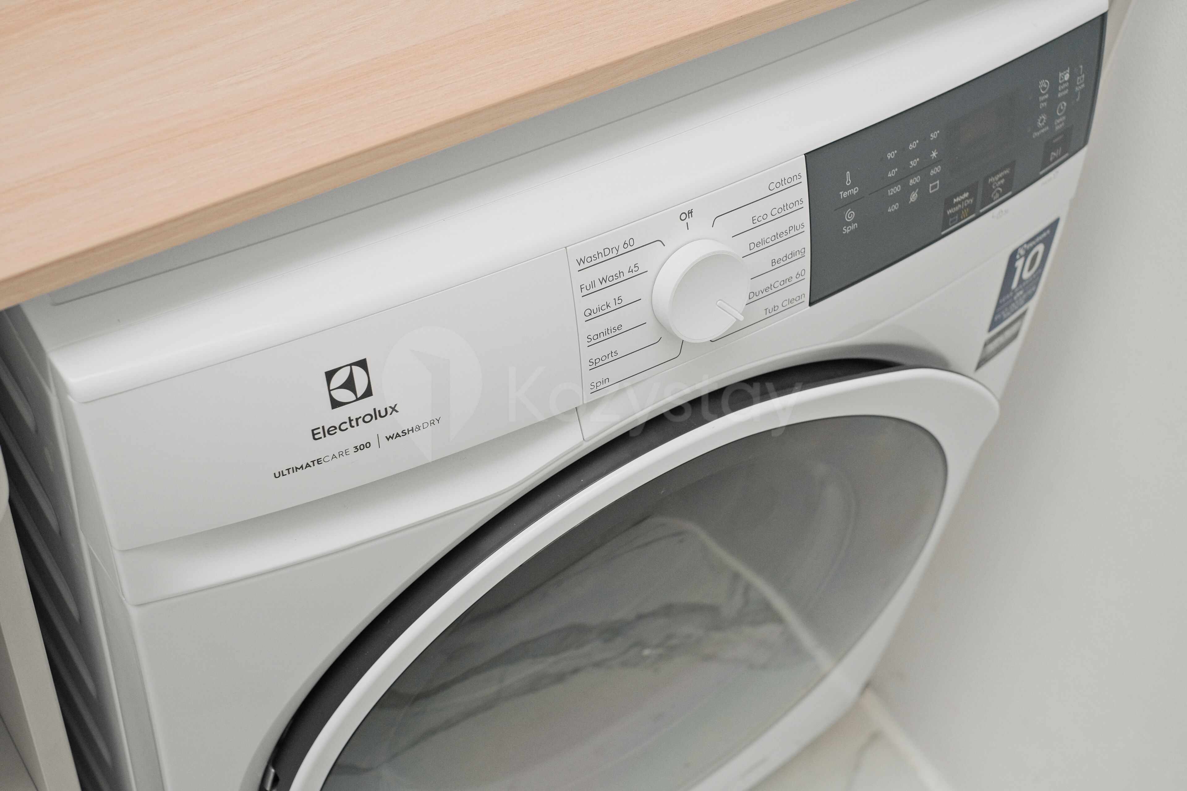 A front view of a washing machine with a control panel and a wooden countertop above it.
