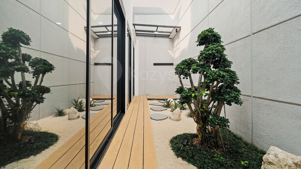 Un jardin intérieur moderne avec un chemin en bois, des plantes en pot et une porte en verre donnant sur un autre espace.