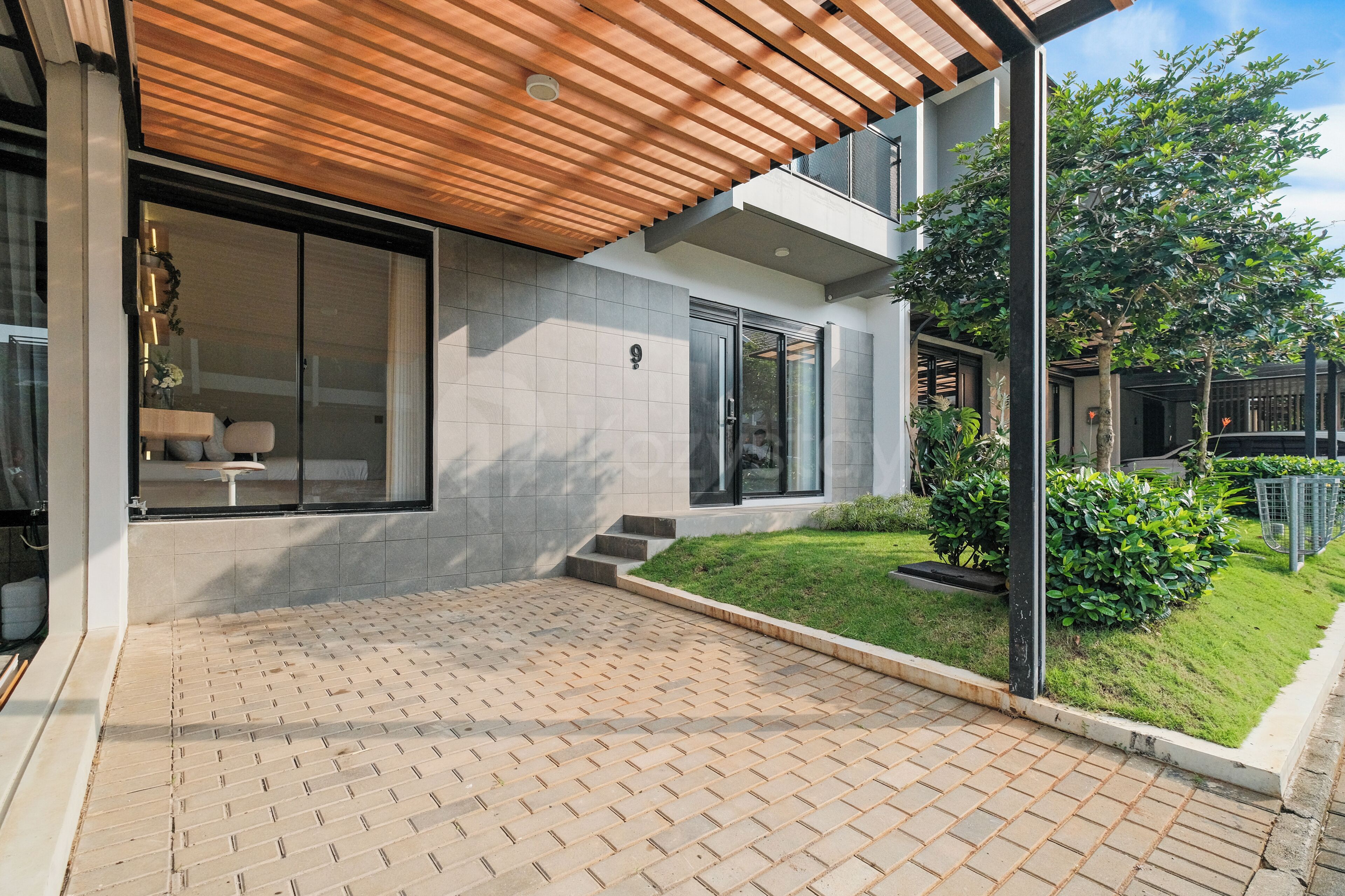 A modern house with a tiled patio, a wooden pergola, and a well-maintained garden.
