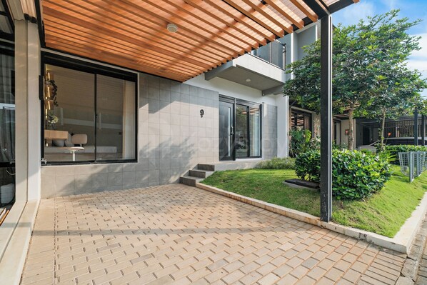A modern house with a tiled patio, a wooden pergola, and a well-maintained garden.