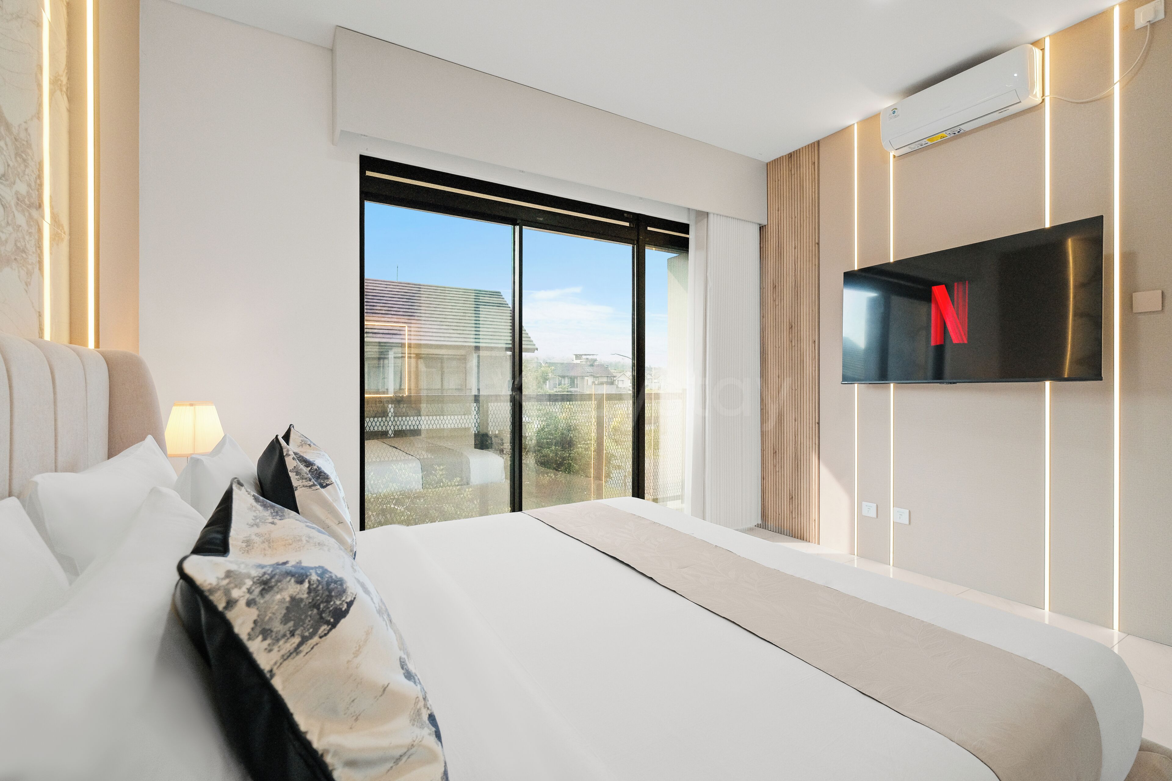 Une chambre d’hôtel moderne dotée d’un grand lit, d’un téléviseur à écran plat fixé au mur et offrant une vue sur l’extérieur grâce à une porte-fenêtre coulissante.
