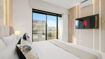 Une chambre d’hôtel moderne dotée d’un grand lit, d’un téléviseur à écran plat fixé au mur et offrant une vue sur l’extérieur grâce à une porte-fenêtre coulissante.
