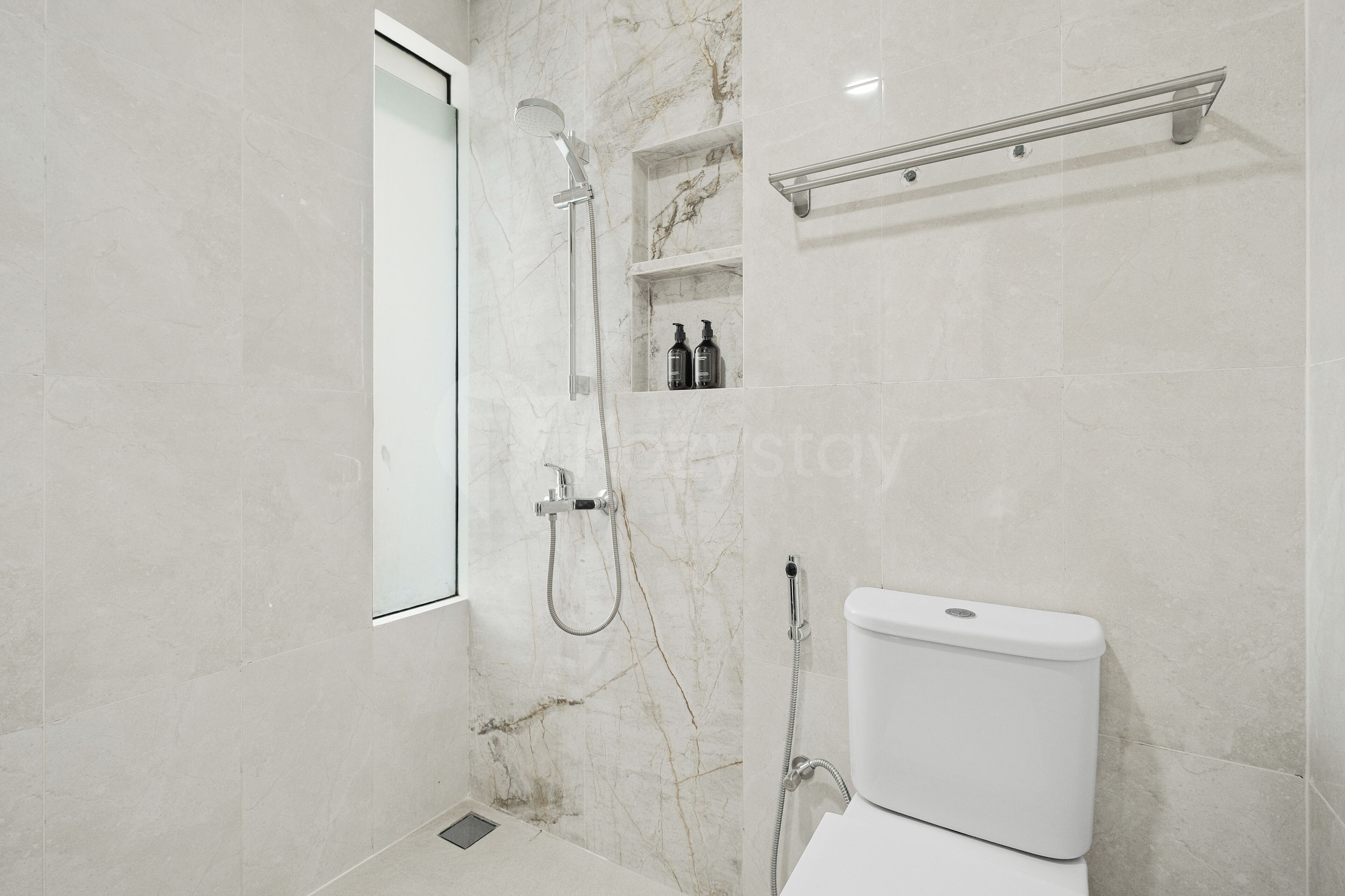 Un baño moderno con ducha, inodoro y un estante con artículos de aseo.